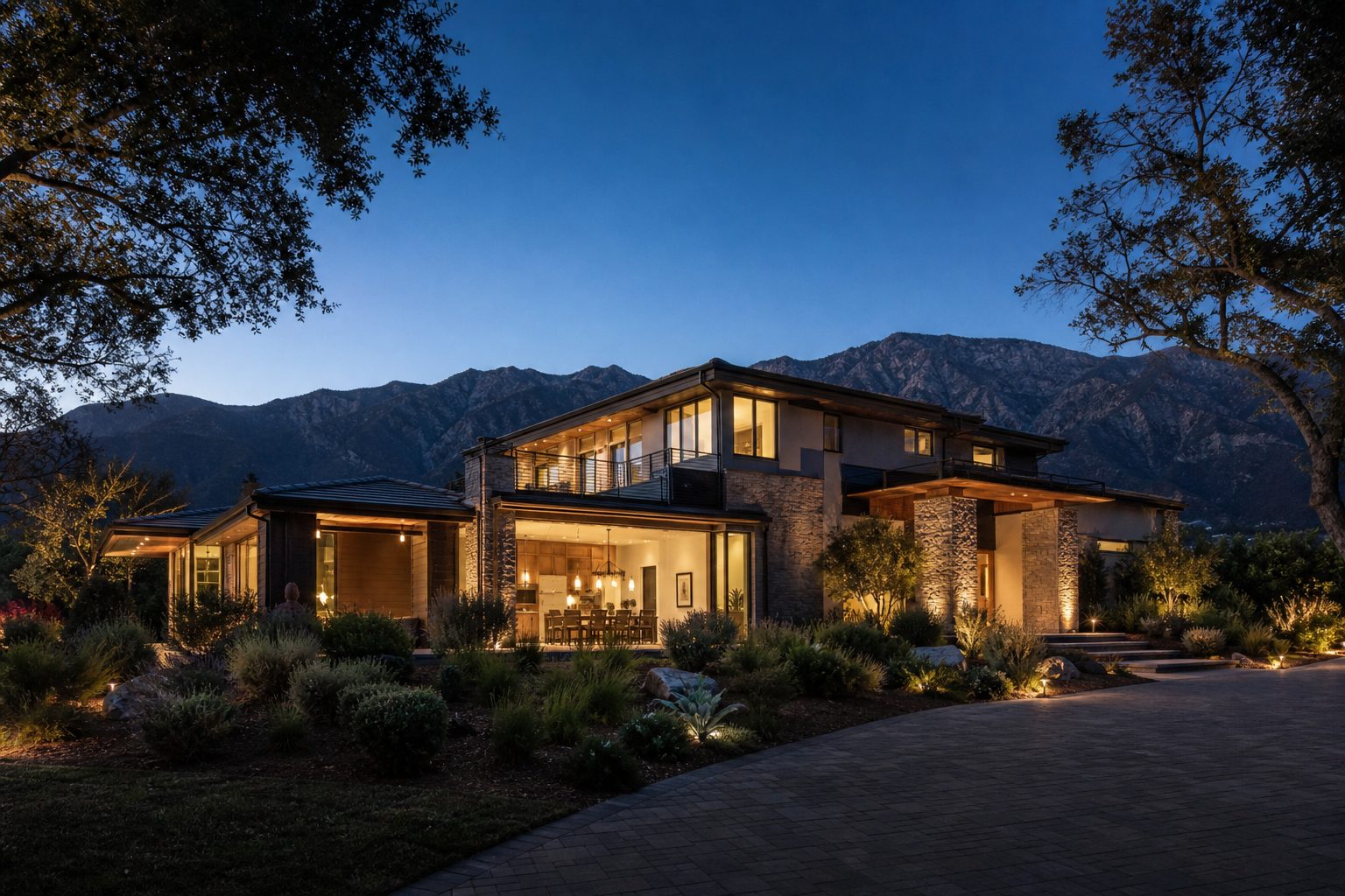 Modern luxury home with interior lights glowing at twilight on foothills lot near North Etiwanda with mountain backdrop.