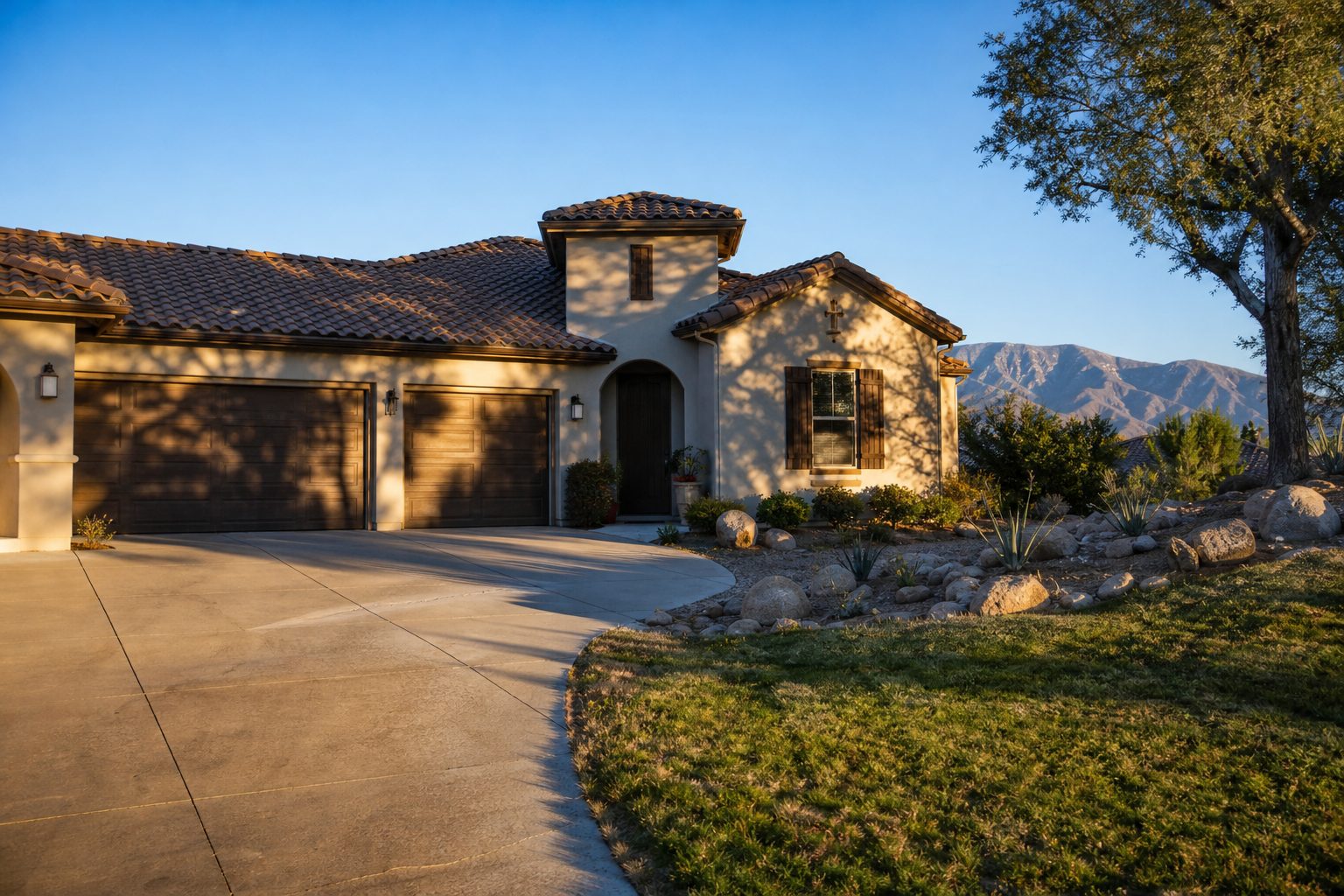 Single-story Etiwanda home with stucco facade, tile roof, and native landscaping in afternoon sunlight on sloped lot with distant mountain view.